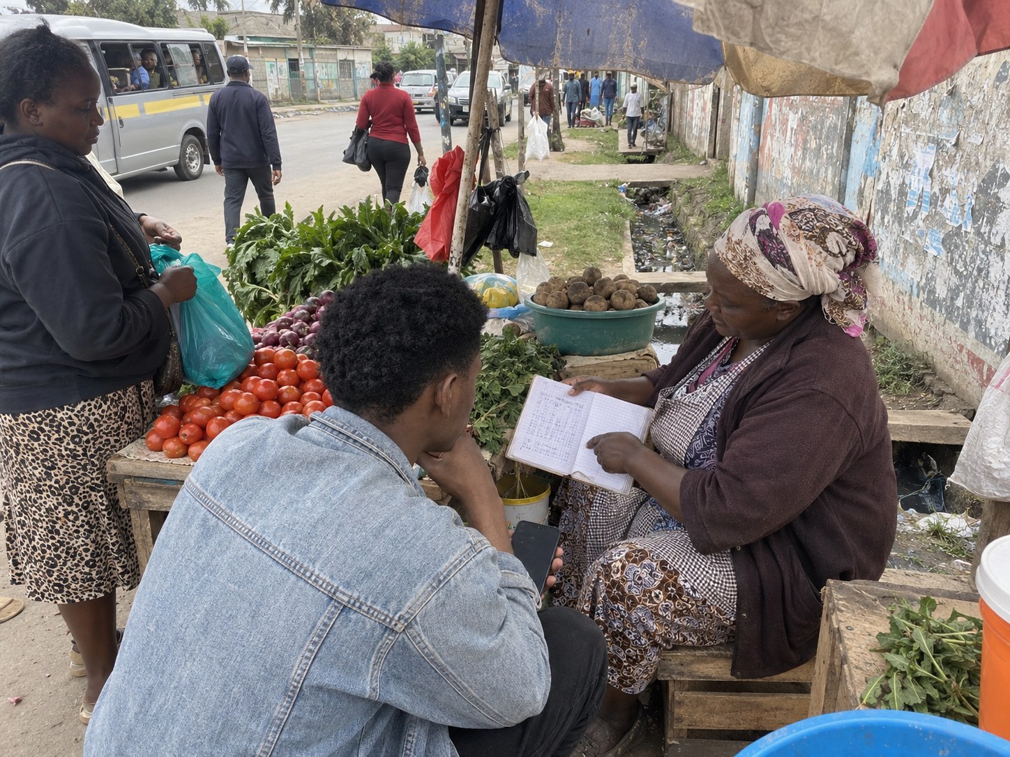 A vegetable seller showing a founder the book where she records what customers owe