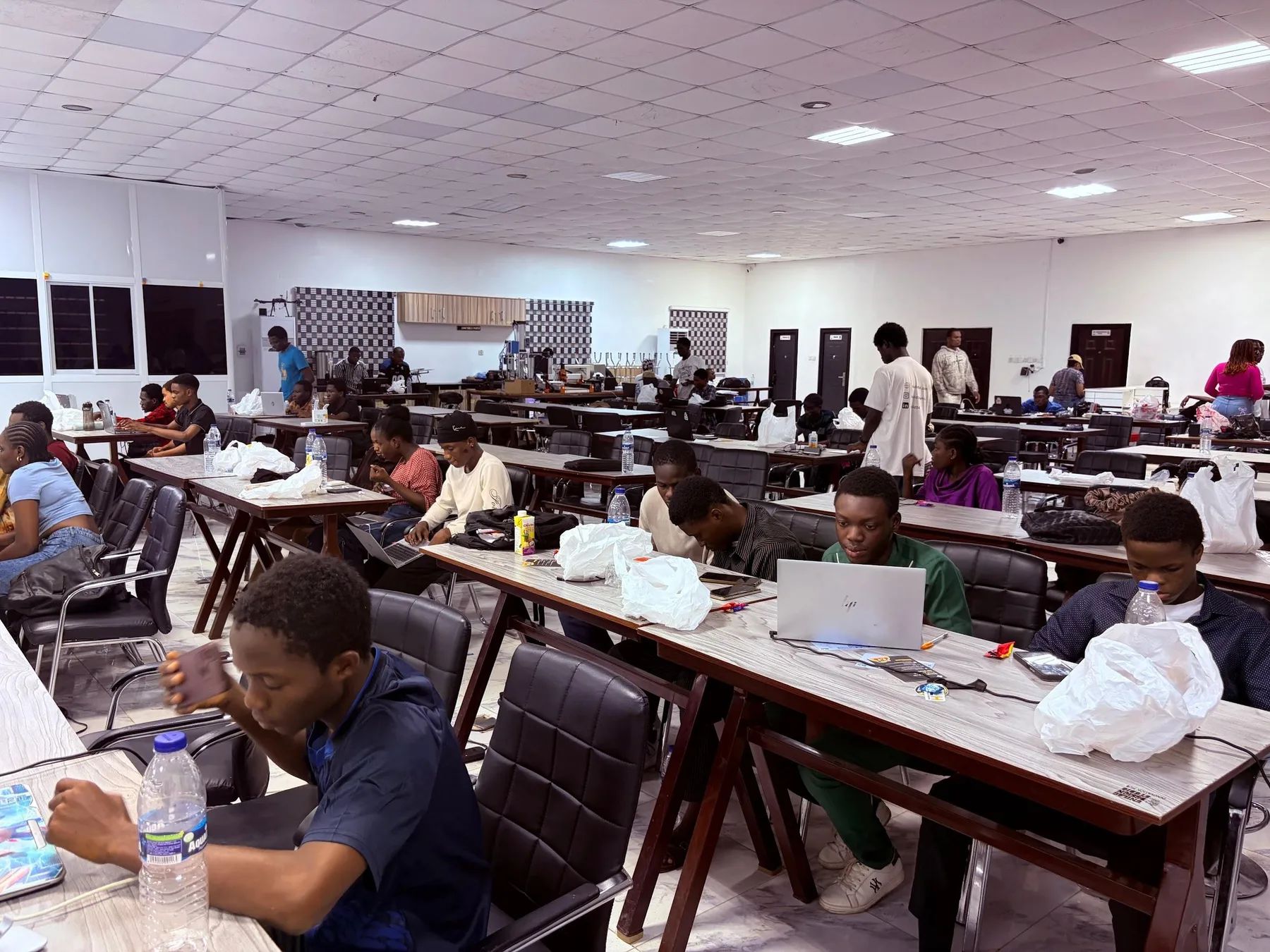 Builders working at laptops along rows of shared tables in a long, bright room